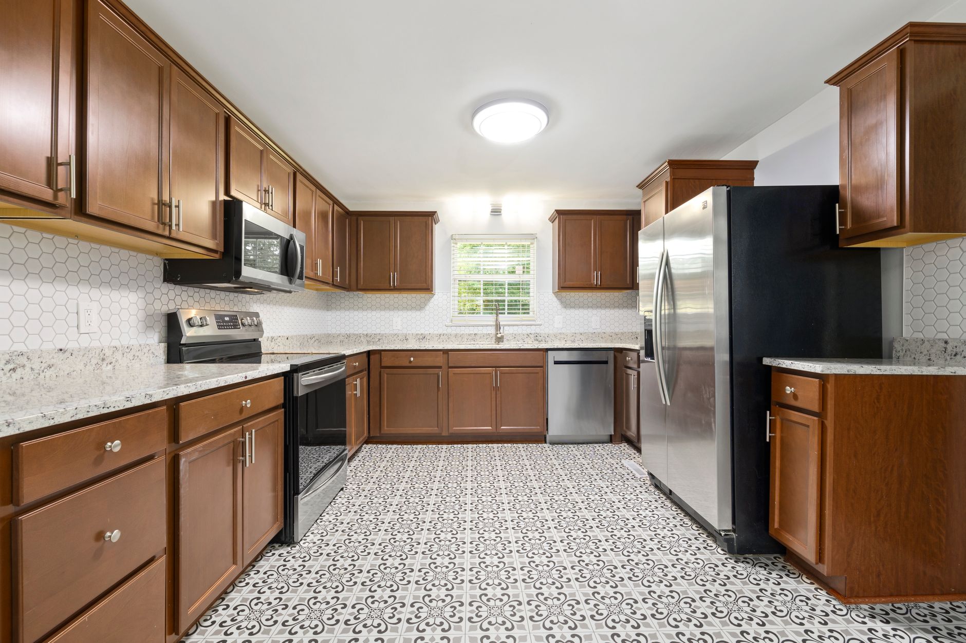 Spacious modern kitchen featuring wooden cabinets, unique tiled floor, and stainless steel appliances in Riverside, CA